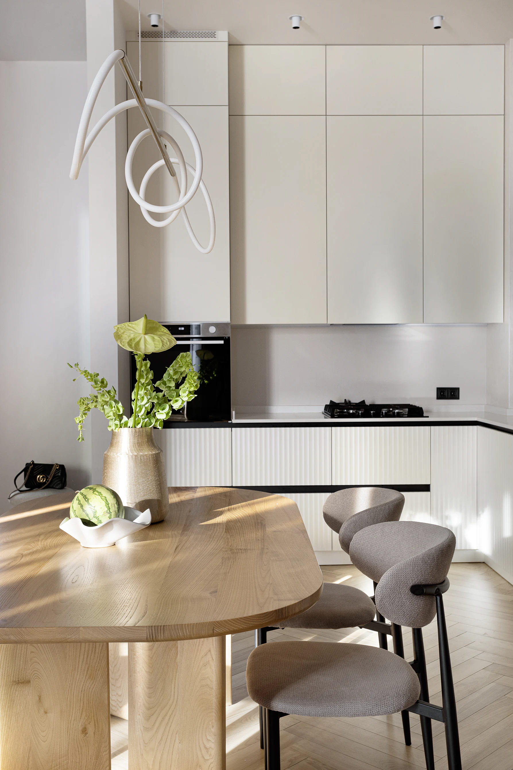 Arcus finished kitchen—oak table with three chairs and vase, loop pendant, tall cream cabinets, built-in oven and gas cooktop