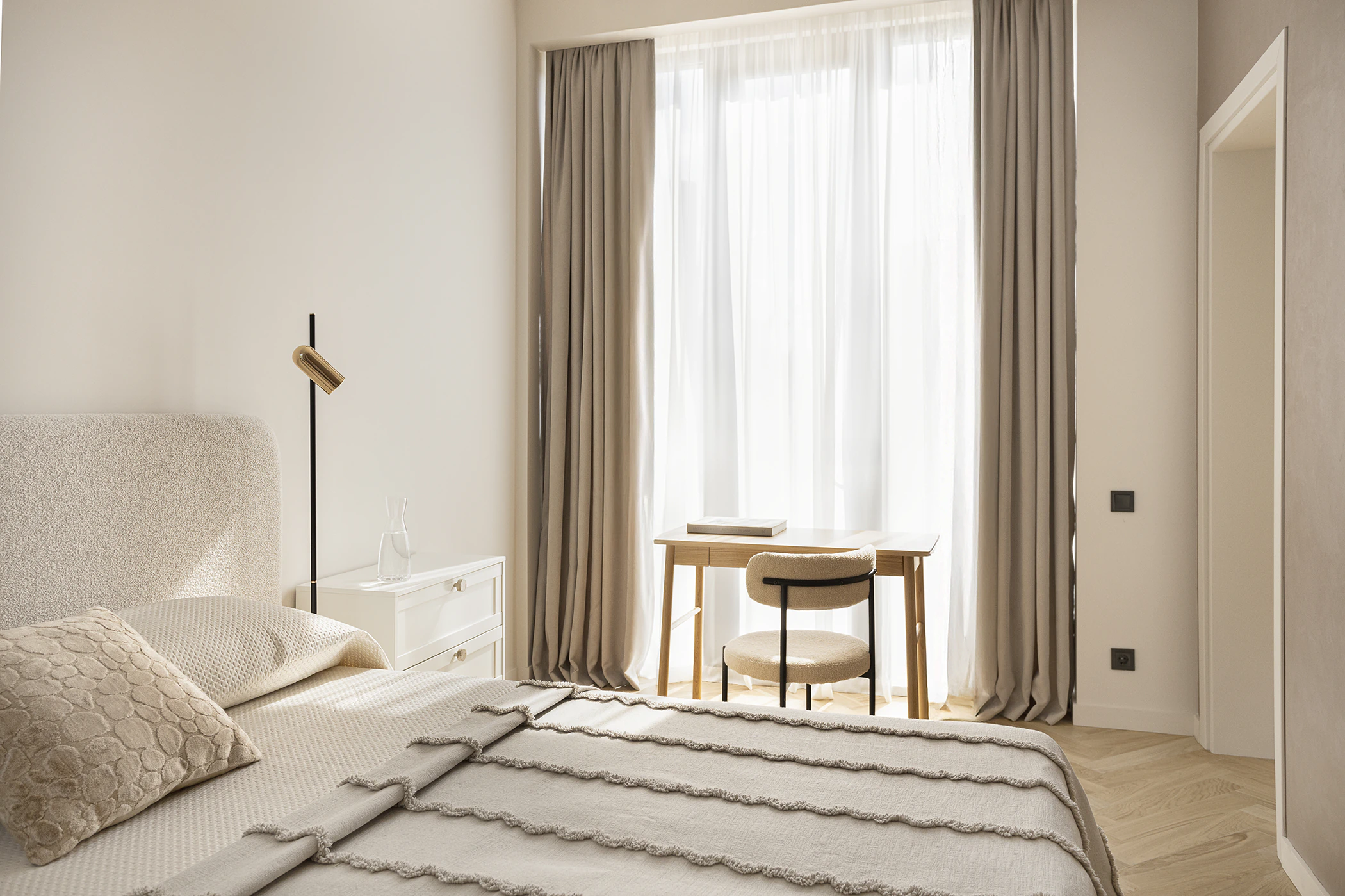 Arcus finished living room—beige sofa, rust swivel armchair, black nesting tables, globe chandelier, abstract art, herringbone floor