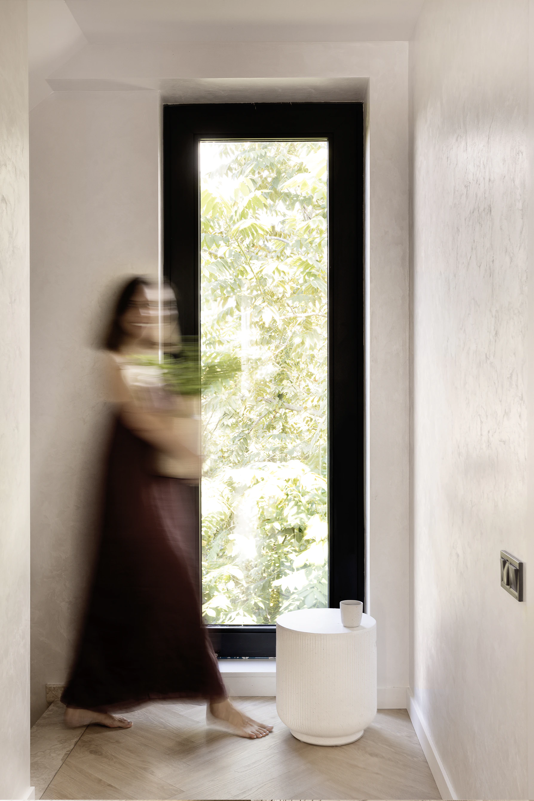 Arcus finished corridor—tall narrow window with greenery, white ribbed side table with cup