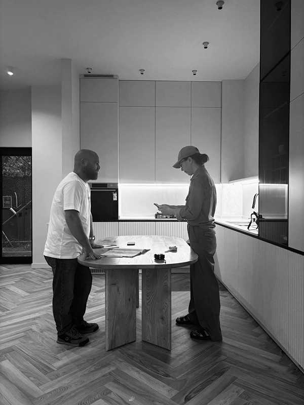 Final touches at Habibi by Arcus, team lead talks with a worker at a round wood table; finished kitchen with LED backsplash and herringbone floor loading=