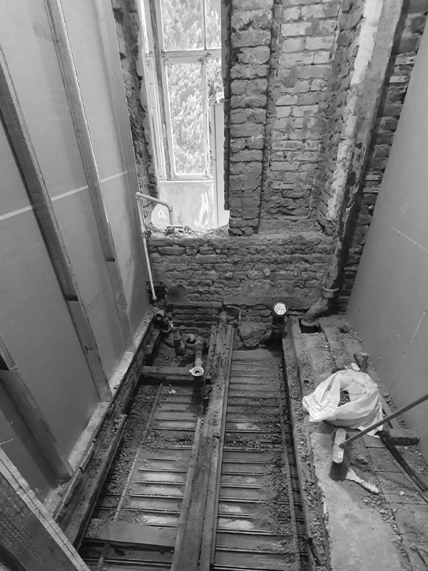Stripped-down bathroom during demolition phase, exposing brick walls and wooden subfloor — renovation by Arcus